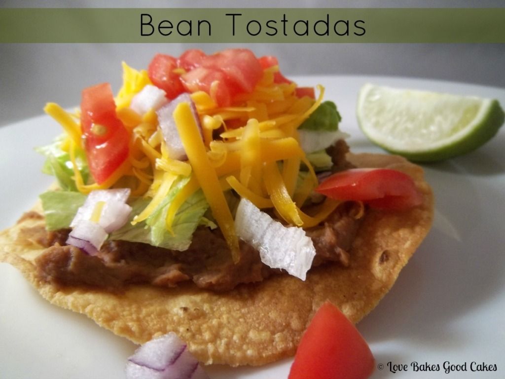 Bean Tostadas with red tomatoes and a slice of lime on a white plate.
